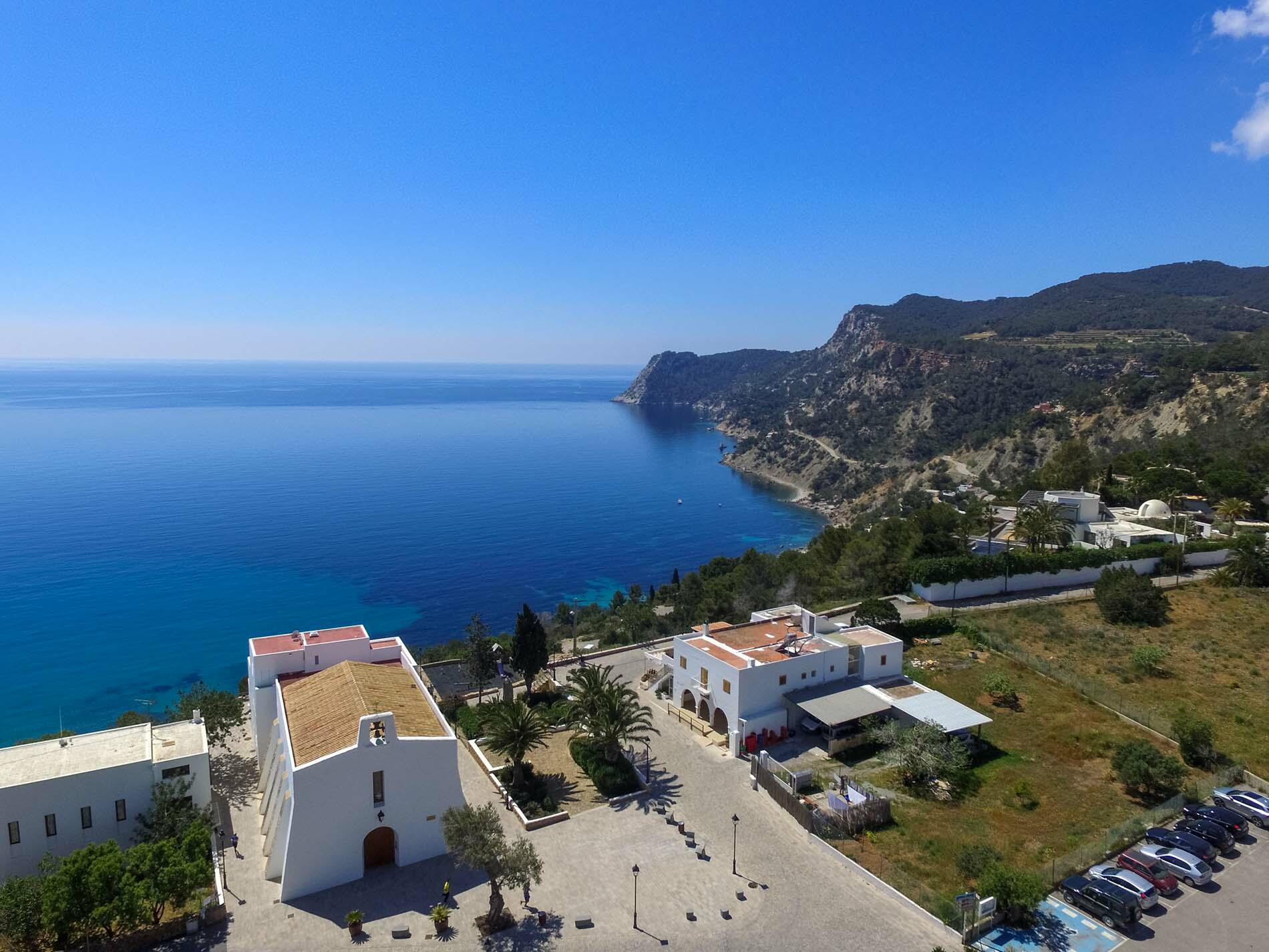 Erhöhte Ansicht von Es Cubells, Ibiza, mit einer weiß getünchten Kirche mit Blick auf das blaue Meer und die zerklüftete Küste