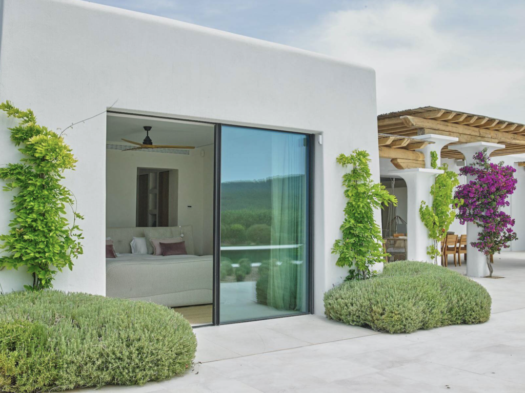 Blakstad Villa auf Ibiza mit weiß getünchten Wänden, Glasschiebetüren, angelegtem Garten und überdachter Terrasse.